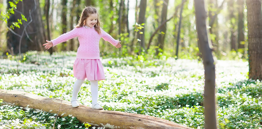 Ein Mädchen mit rosafarbenen Kleid balanciert auf einem Baumstamm in einem Wald im Frühlung