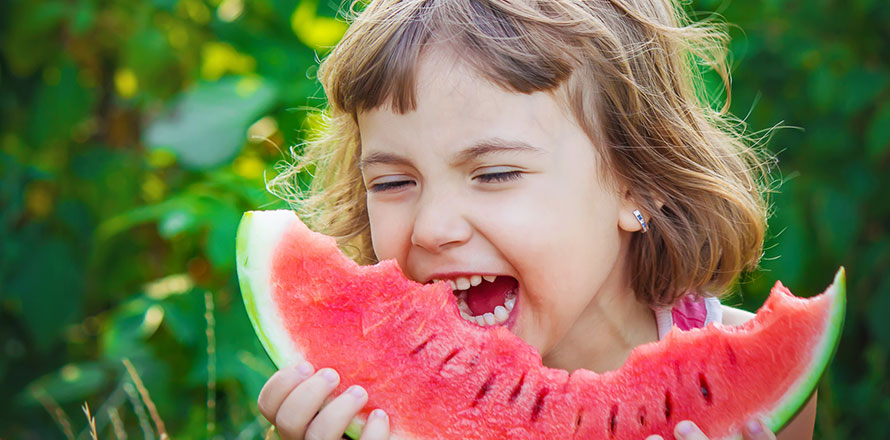 Mädchen beisst lachend in ein Stück Wassermelone