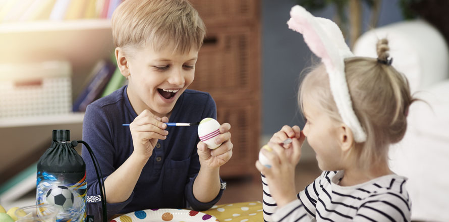 Zwei Kinder bemalen Ostereier an einem Tisch