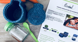 Emeal Babybreibehälter mit Löffel und Thermobecher auf einem Tisch
